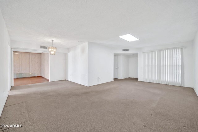 carpeted spare room featuring a textured ceiling and a notable chandelier