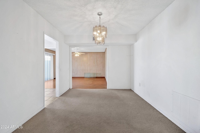 carpeted spare room with ceiling fan with notable chandelier and a textured ceiling