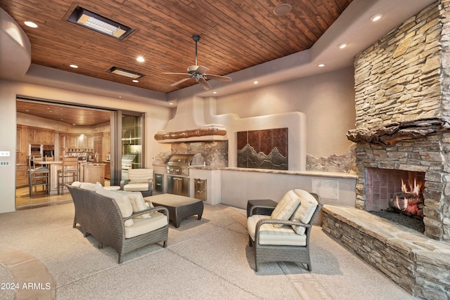 living room with a stone fireplace, a tray ceiling, and wooden ceiling