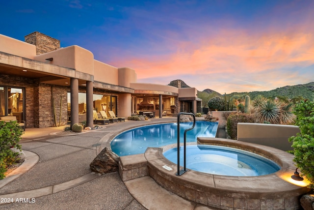 pool at dusk featuring a patio area and an in ground hot tub