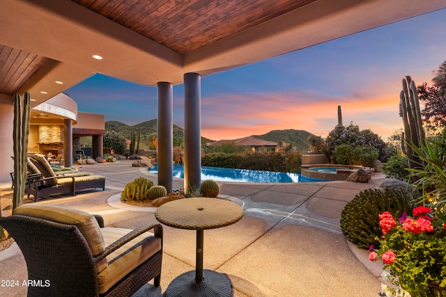 patio terrace at dusk featuring a mountain view and a swimming pool with hot tub