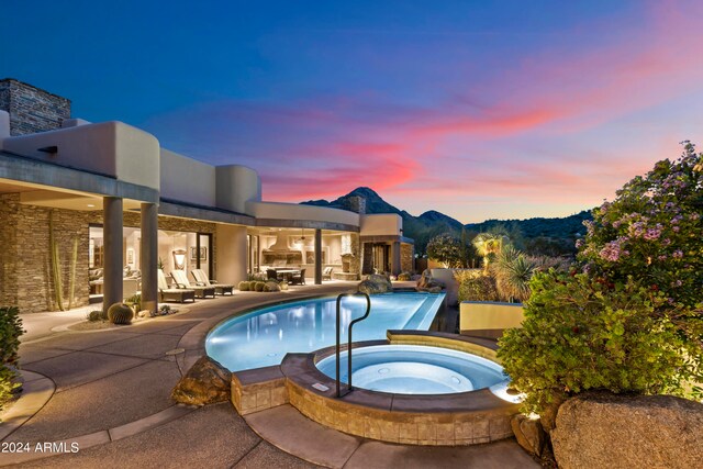 pool at dusk featuring an in ground hot tub and a patio