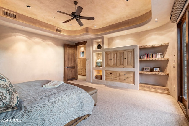 bedroom with ceiling fan, a tray ceiling, and light carpet