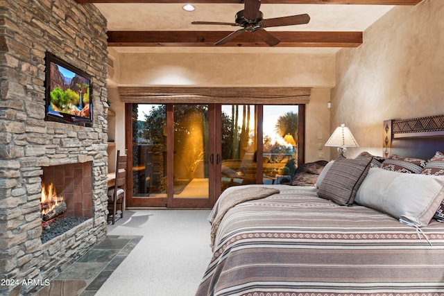 bedroom with dark carpet, beamed ceiling, ceiling fan, access to exterior, and a stone fireplace