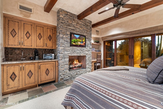 bedroom featuring beam ceiling, dark tile flooring, sink, a stone fireplace, and french doors