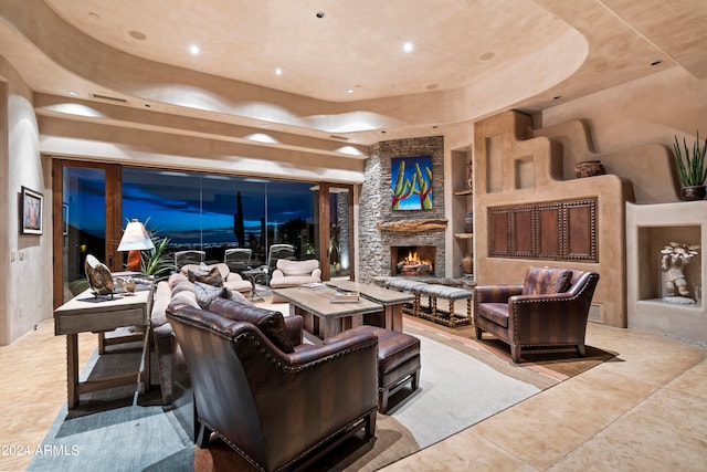 interior space featuring a stone fireplace, built in shelves, light tile floors, and a raised ceiling