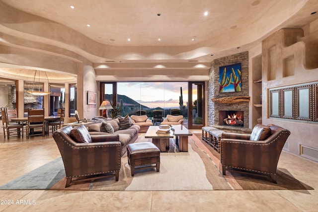 tiled living room featuring a raised ceiling and a stone fireplace