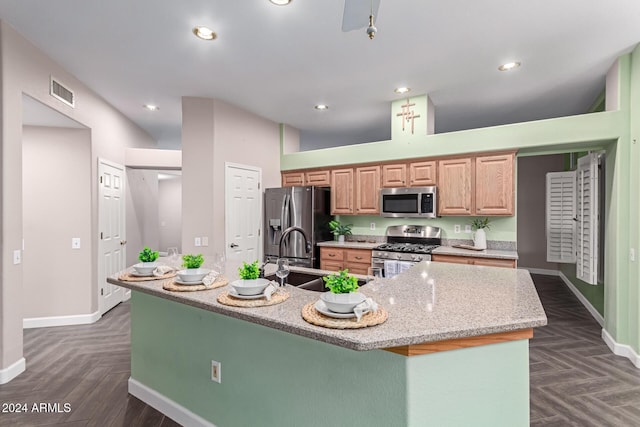 kitchen featuring light brown cabinetry, dark parquet floors, stainless steel appliances, sink, and an island with sink