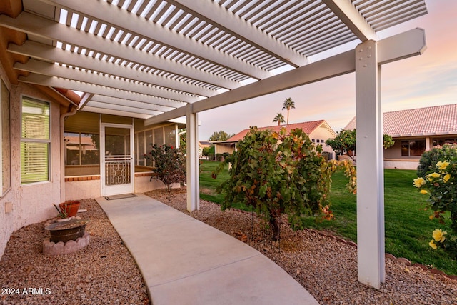 patio terrace at dusk featuring a pergola and a yard