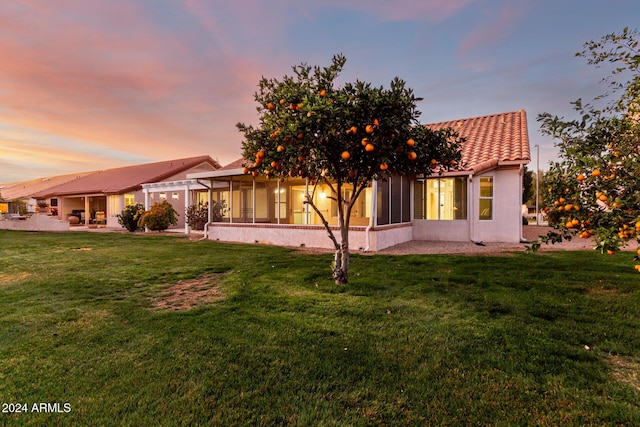 back house at dusk with a yard and a sunroom