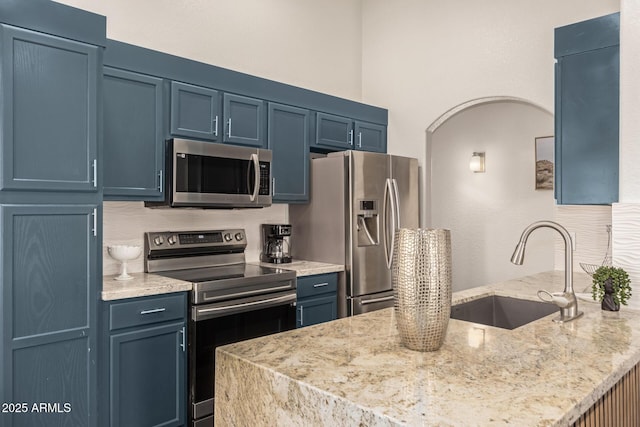 kitchen featuring arched walkways, a peninsula, blue cabinetry, a sink, and stainless steel appliances