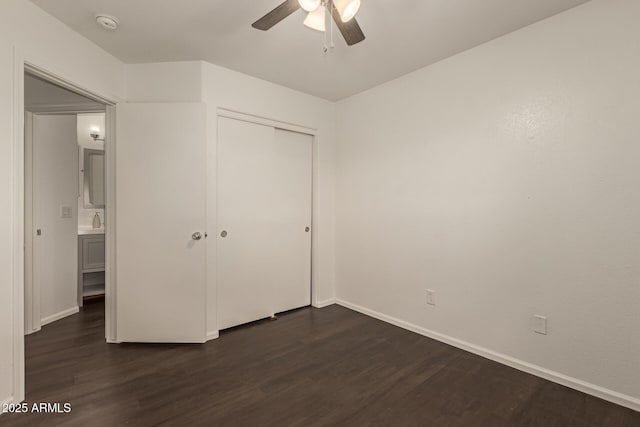 unfurnished bedroom with dark wood-style flooring, a closet, baseboards, a ceiling fan, and a sink