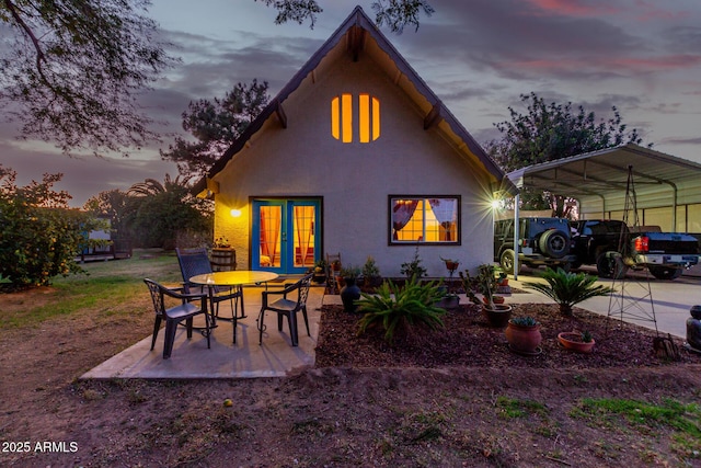 back house at dusk with french doors and a carport