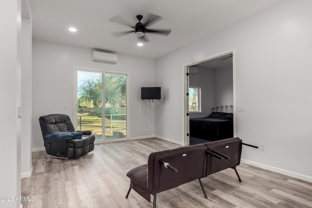 living area featuring ceiling fan, light wood-type flooring, and a wall mounted AC