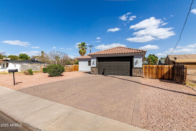 view of front facade featuring fence, a tile roof, stucco siding, decorative driveway, and stone siding