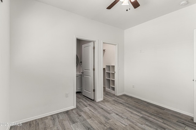 unfurnished bedroom with a walk in closet, wood finished floors, a closet, baseboards, and ceiling fan