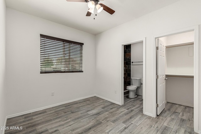 unfurnished bedroom with a walk in closet, baseboards, wood finished floors, a closet, and ensuite bath