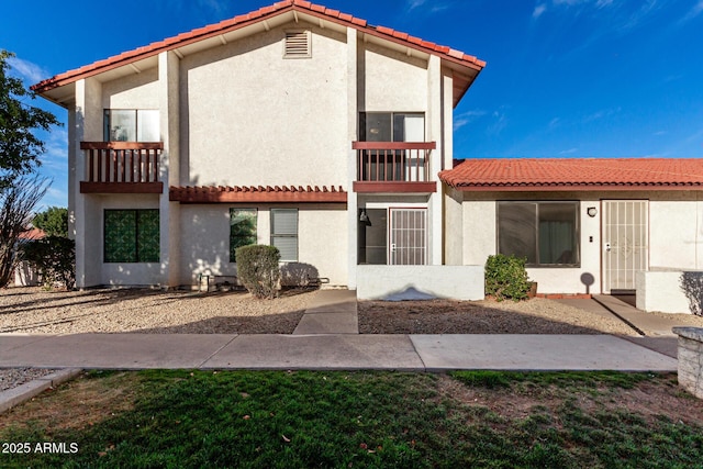 back of property with a tile roof, a balcony, and stucco siding