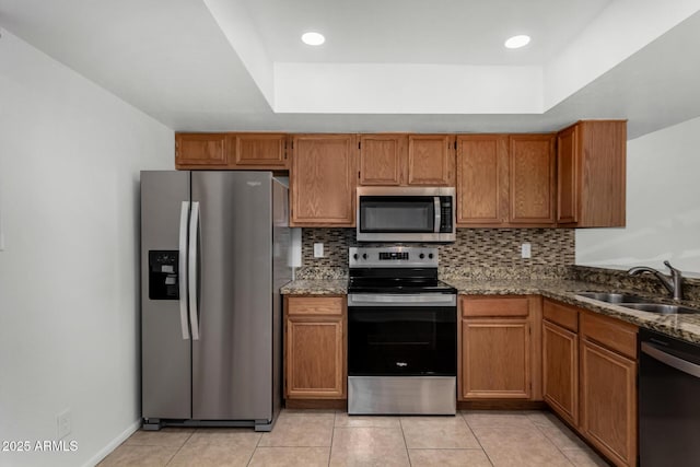 kitchen featuring stainless steel appliances, a tray ceiling, a sink, and tasteful backsplash