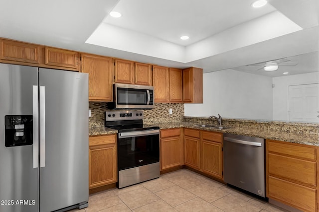 kitchen with a sink, appliances with stainless steel finishes, dark stone counters, tasteful backsplash, and a raised ceiling