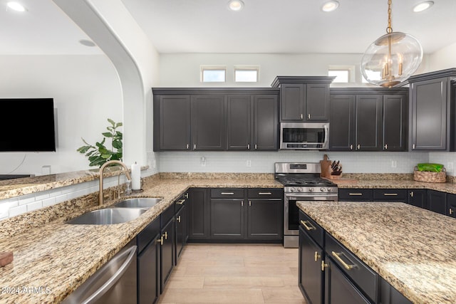 kitchen with light stone counters, sink, pendant lighting, and appliances with stainless steel finishes