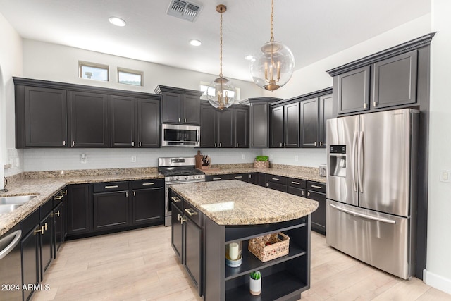 kitchen with appliances with stainless steel finishes, light stone counters, decorative light fixtures, light hardwood / wood-style floors, and a kitchen island