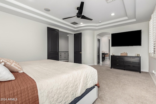 bedroom with a raised ceiling, ceiling fan, and light colored carpet