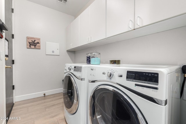 clothes washing area featuring cabinets, light wood-type flooring, and washer and clothes dryer