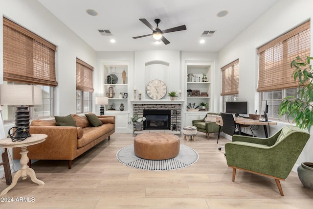 living room featuring a brick fireplace, built in shelves, ceiling fan, and light hardwood / wood-style flooring