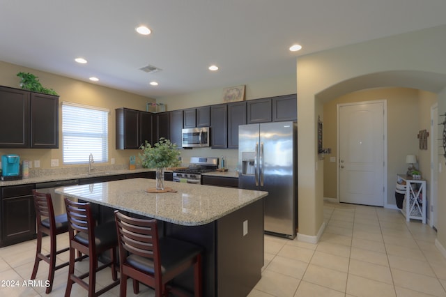 kitchen with light tile patterned flooring, a kitchen island, stainless steel appliances, and light stone counters