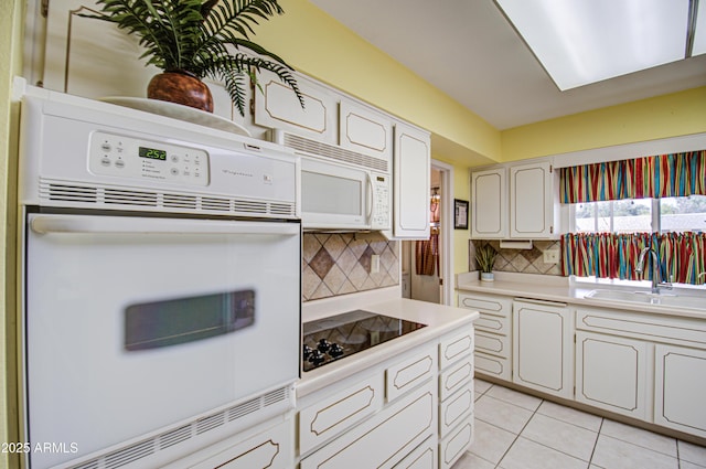 kitchen featuring light tile patterned floors, tasteful backsplash, light countertops, a sink, and white appliances