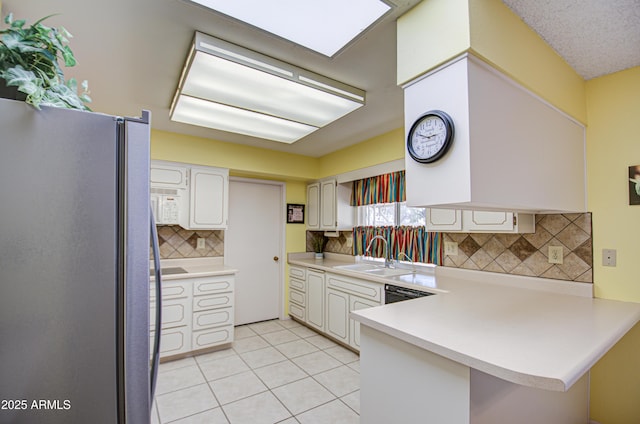 kitchen featuring light tile patterned floors, light countertops, freestanding refrigerator, a sink, and a peninsula