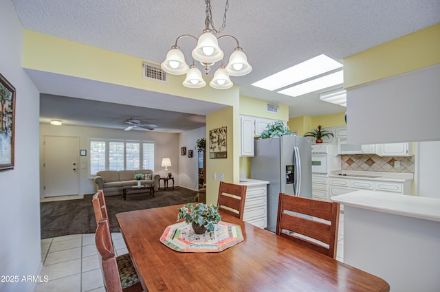 dining space featuring a skylight, light tile patterned floors, visible vents, a textured ceiling, and ceiling fan with notable chandelier