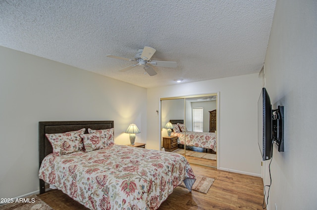 bedroom with baseboards, a ceiling fan, wood finished floors, a textured ceiling, and a closet