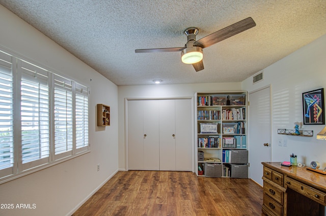 interior space featuring a textured ceiling, ceiling fan, wood finished floors, and visible vents