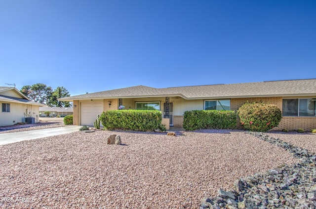 ranch-style home with brick siding, a shingled roof, concrete driveway, central AC unit, and a garage