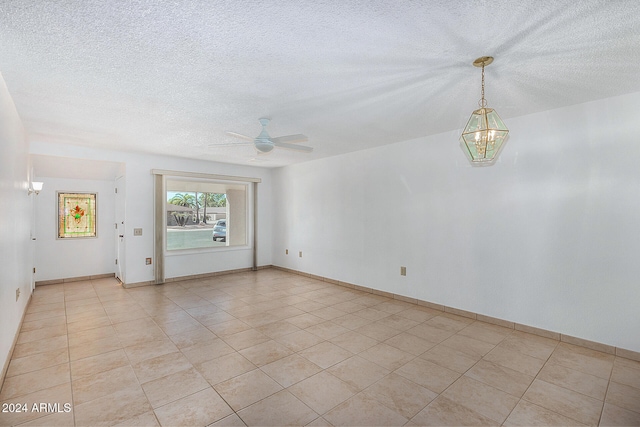 tiled spare room with a textured ceiling and ceiling fan with notable chandelier