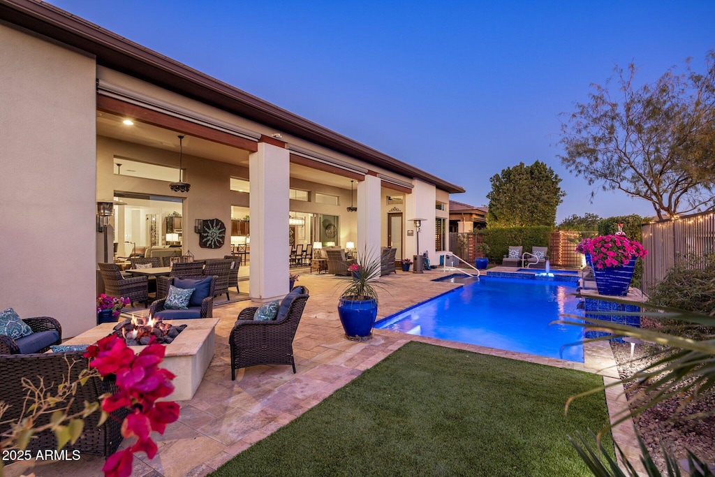 pool at dusk with pool water feature, a patio area, and an outdoor living space with a fire pit