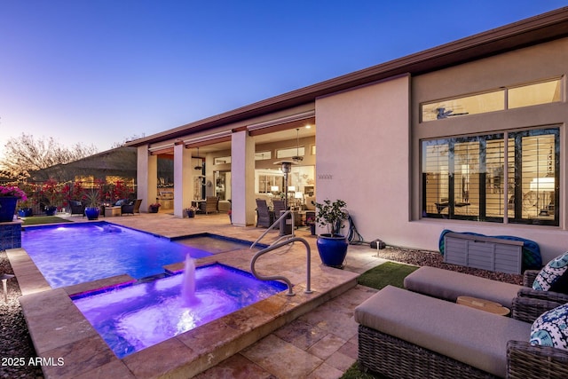 pool at dusk with pool water feature, an in ground hot tub, and a patio