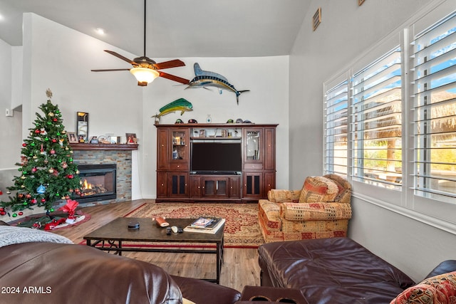 living room with lofted ceiling, ceiling fan, a stone fireplace, and wood-type flooring