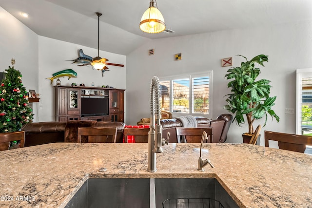 kitchen with ceiling fan, light stone counters, lofted ceiling, and sink