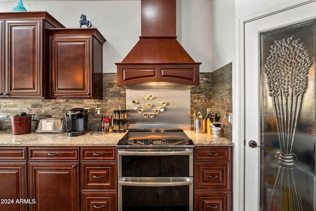 kitchen featuring stainless steel range oven, premium range hood, and tasteful backsplash