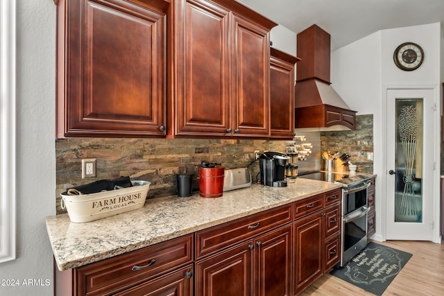 kitchen featuring double oven range, light stone counters, light hardwood / wood-style floors, and ventilation hood