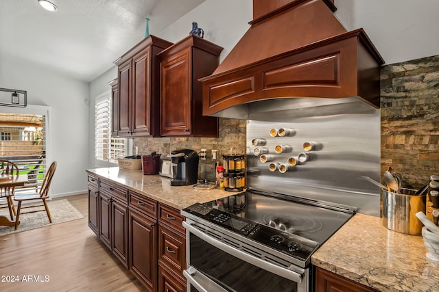 kitchen featuring custom exhaust hood, vaulted ceiling, electric range, light wood-type flooring, and tasteful backsplash