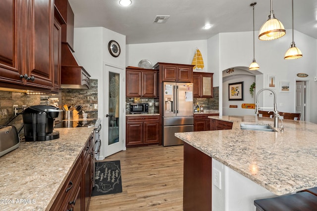 kitchen featuring sink, high end refrigerator, pendant lighting, decorative backsplash, and light wood-type flooring