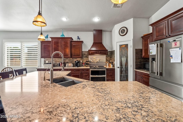 kitchen featuring decorative backsplash, appliances with stainless steel finishes, custom range hood, sink, and pendant lighting