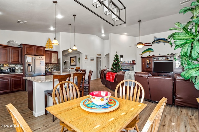 dining area featuring ceiling fan, sink, high vaulted ceiling, light hardwood / wood-style flooring, and a fireplace