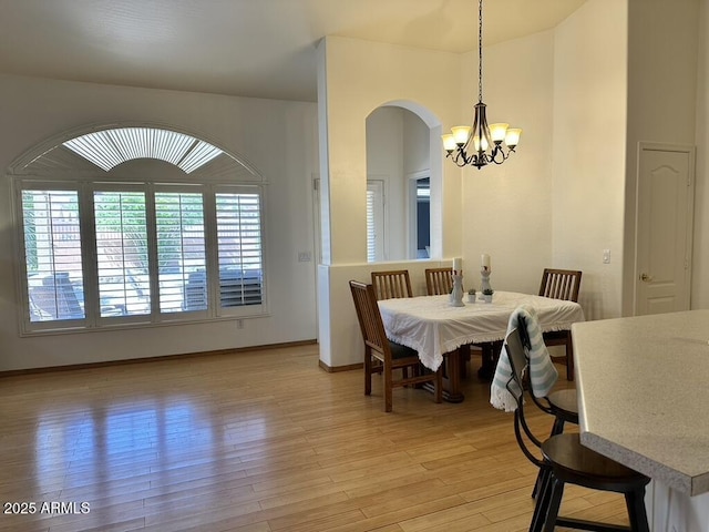 dining area with a chandelier, arched walkways, light wood-style floors, and baseboards