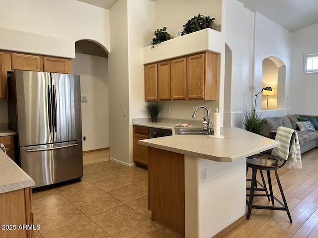 kitchen featuring freestanding refrigerator, a sink, a kitchen bar, arched walkways, and a towering ceiling