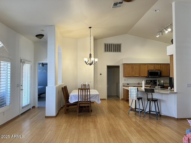kitchen featuring stainless steel microwave, brown cabinetry, a chandelier, plenty of natural light, and high vaulted ceiling
